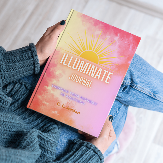 A person holding an open journal titled 'Illuminate Journal' with a colorful, artistic design on the cover.